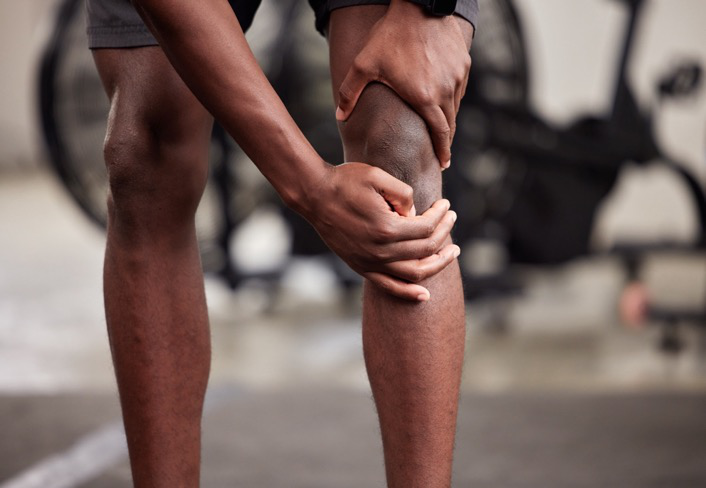 : A Black man holds his knee with both hands as he experiences a knee injury.