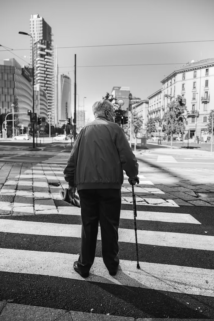 an elderly man using a walking stick to cross the road