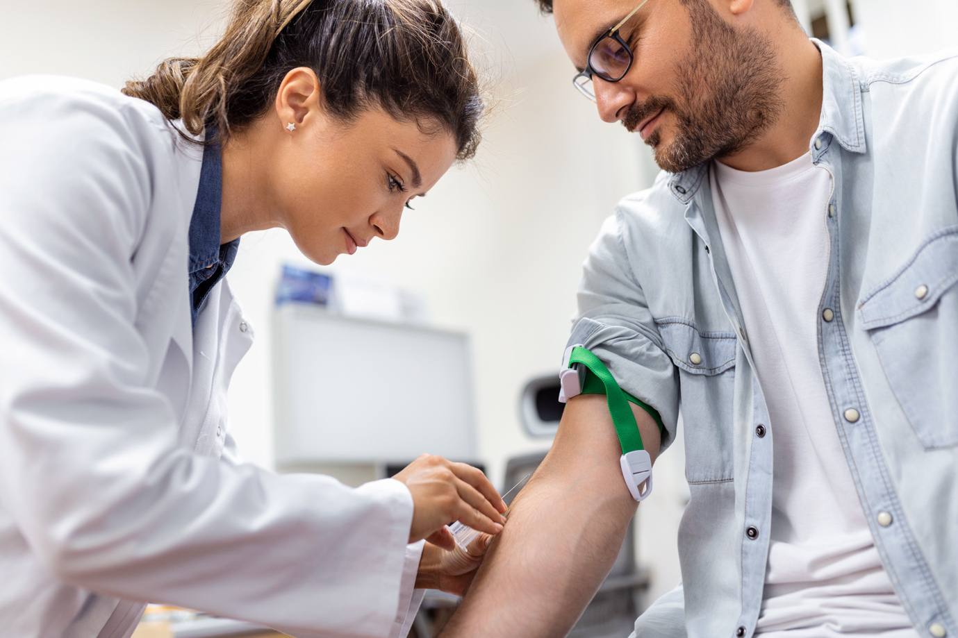 a female phlebotomist in a white coat about to draw blood from a man’s arm