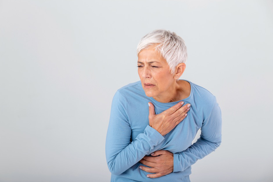 A middle-aged woman in a blue shirt holds her chest in pain.