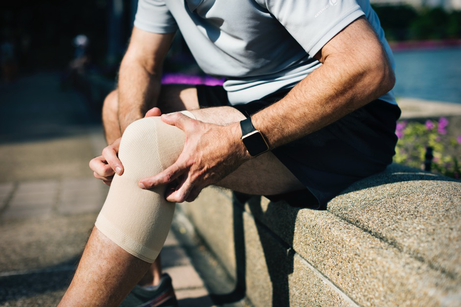 A man sitting on a bench holding his wrapped knee.