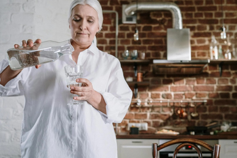 An older woman pouring water into a glass.