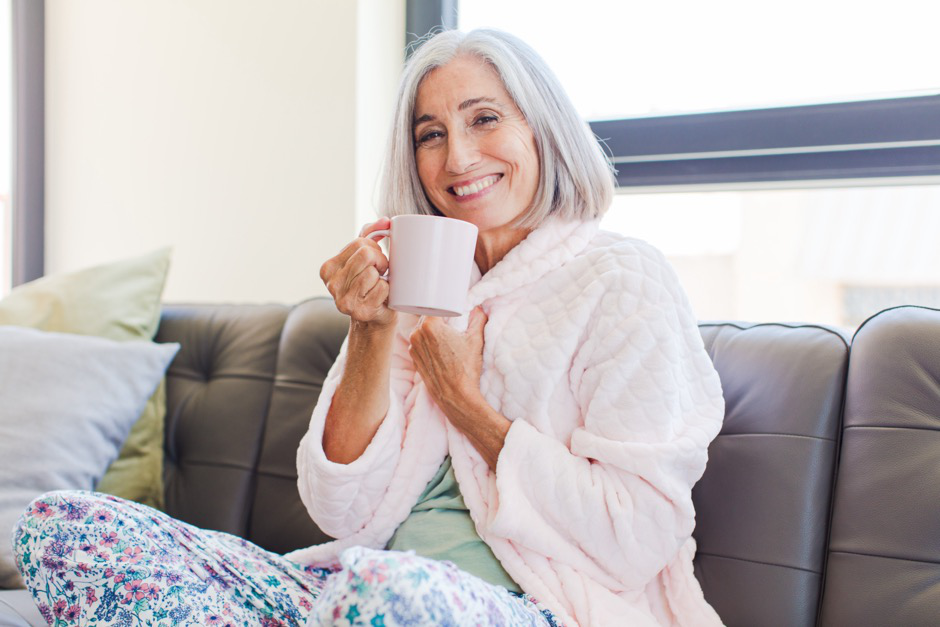 A woman resting on her couch with a cup of tea, focusing on recovery and relaxation after surgery.