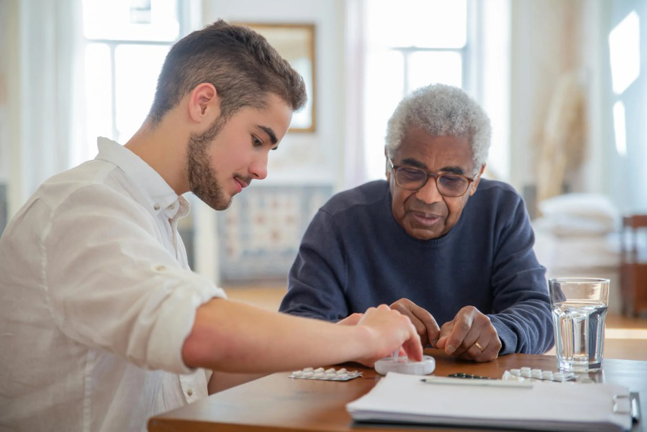 A caregiver assisting an elderly man with taking supplements to support bone and spine health.