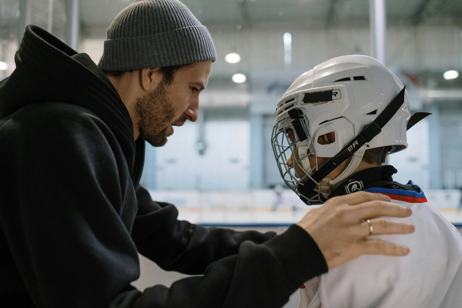 A coach assisting a young athlete during ice hockey practice.