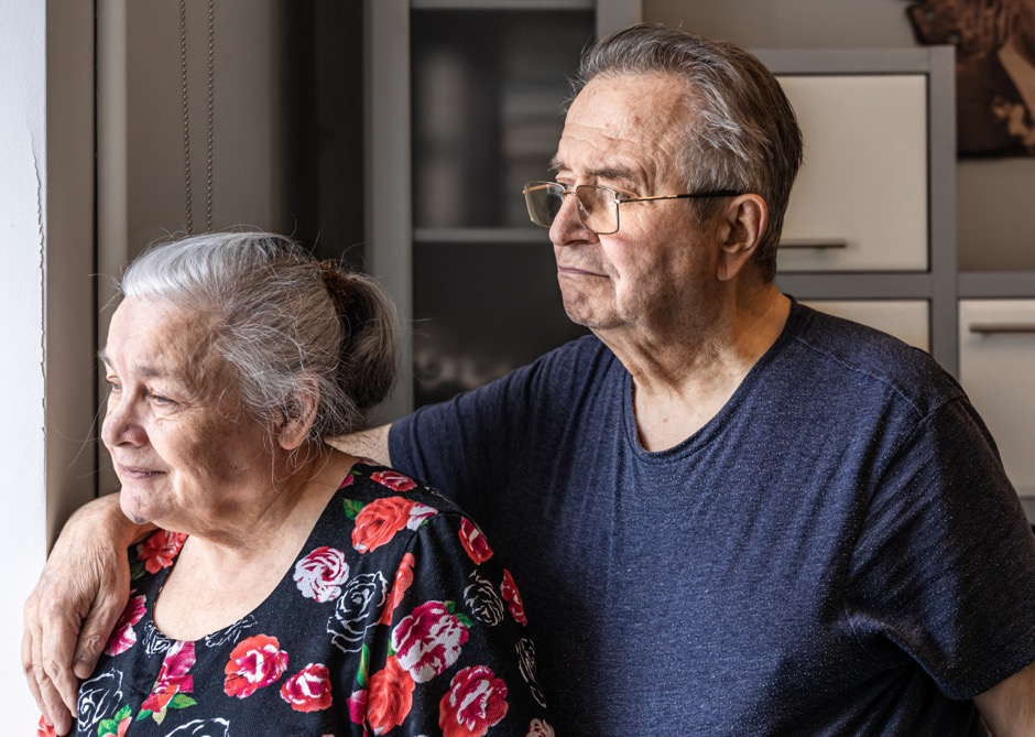 An elderly woman and a man smiling while looking out the window.