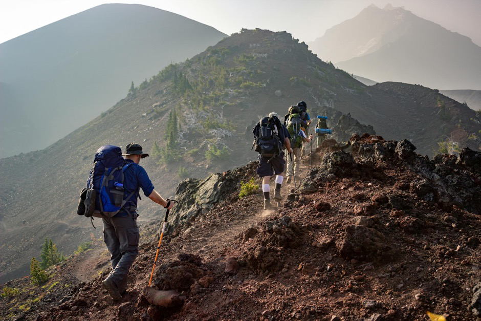 A group of friends hiking on a rugged trail, wearing sturdy hiking boots and using trekking poles.