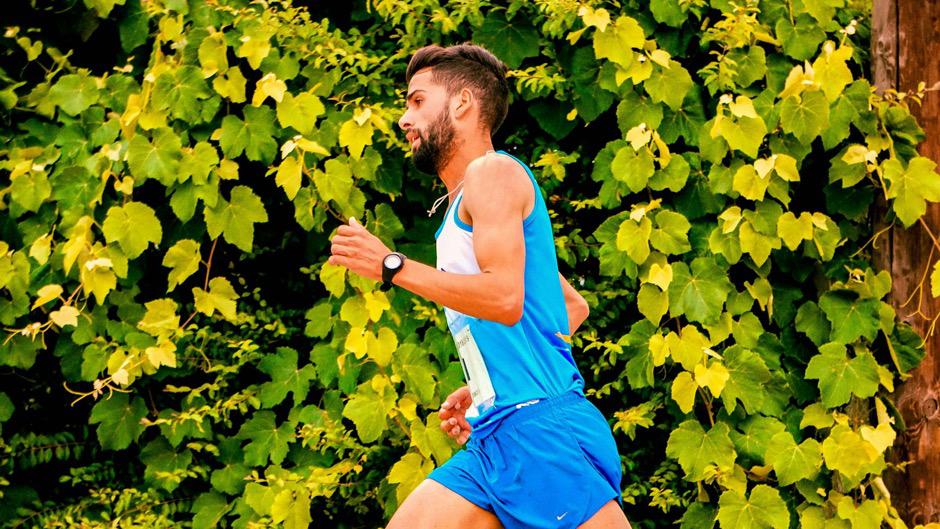 A focused runner moving along a scenic path with vibrant greenery in the background.